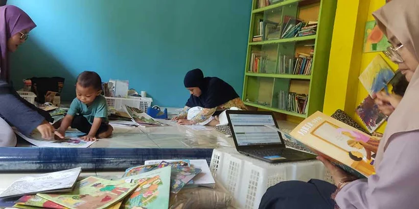 1 November 2023, day 2 librarian training: Nadhif enters bibliographic information into the laptop, while Tika cuts plastic for covering the books. Damar and Ririn were reading books